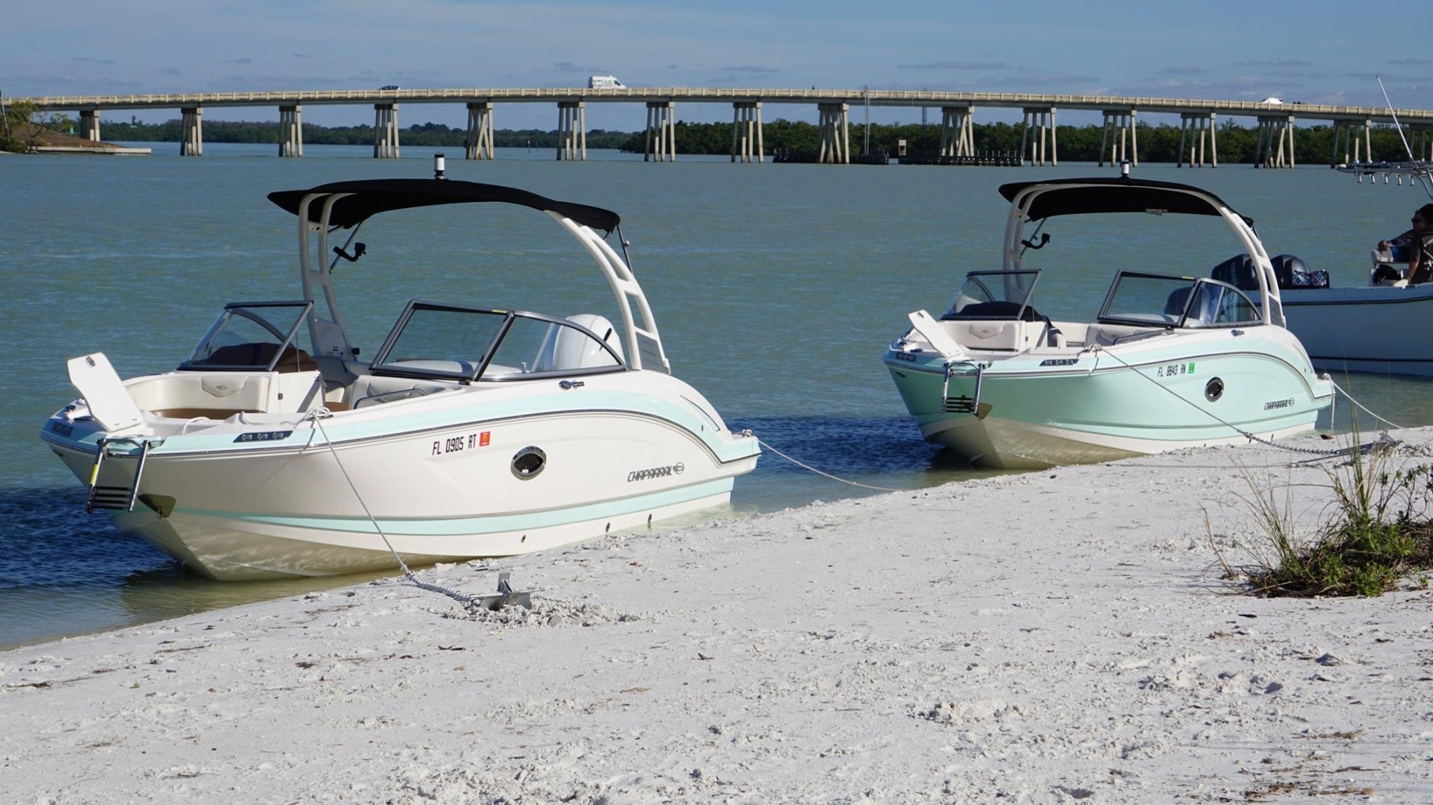 Two anchored boats on sandy shore with bridge in background.