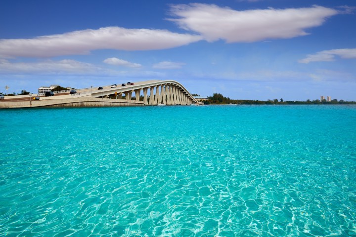 Bridge over vibrant turquoise water with a blue sky and clouds.