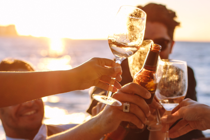 Group of people toasting with drinks at sunset by the ocean.