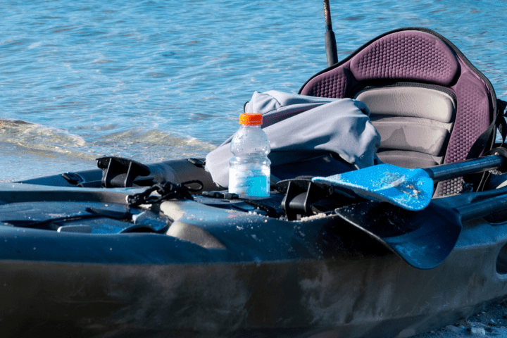 Fishing kayak with gear and paddles on a sandy beach.