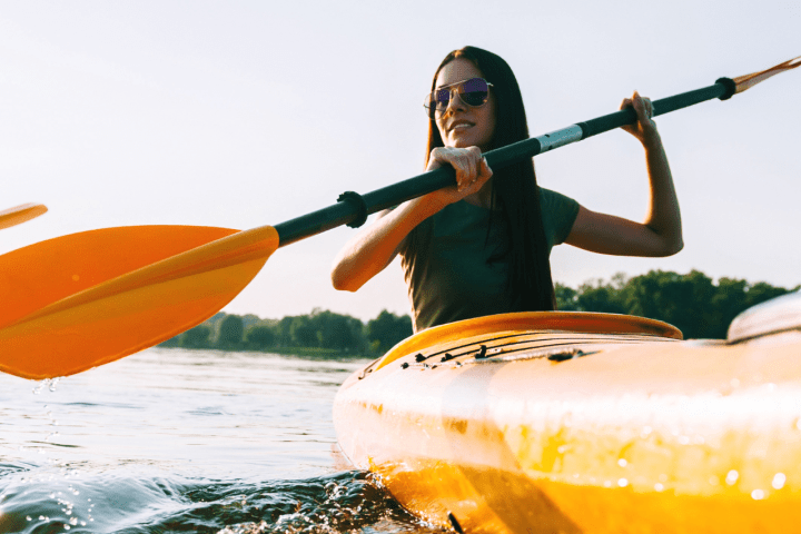 Two people kayaking on a sunny day with trees in the background.