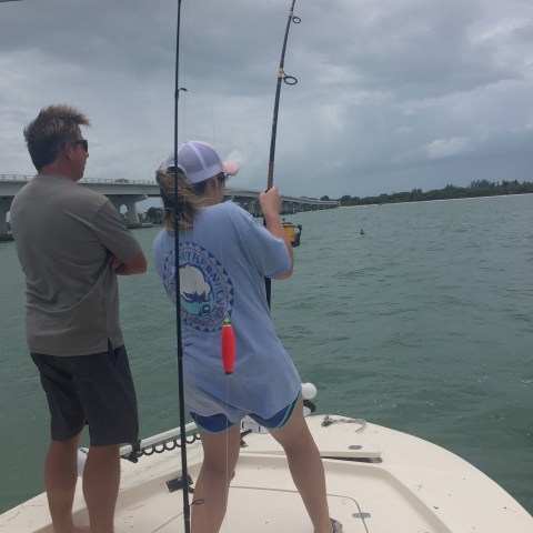 Person fishing from a boat with another person observing nearby.