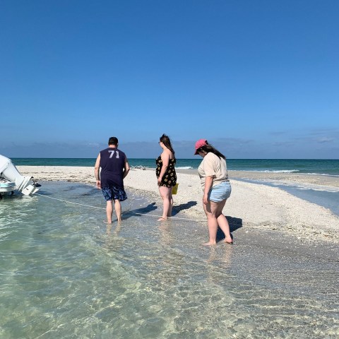 Three people walking on a beach by a small boat in shallow water.