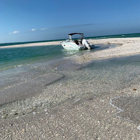 Boat on sandy beach with clear blue sky and ocean.