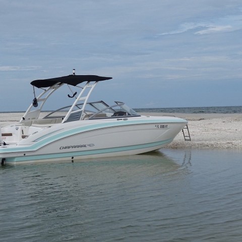 White speedboat anchored on a sandy beach with cloudy sky.